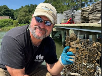 Todd Janeski sits beside a body of water holding an oyster shell